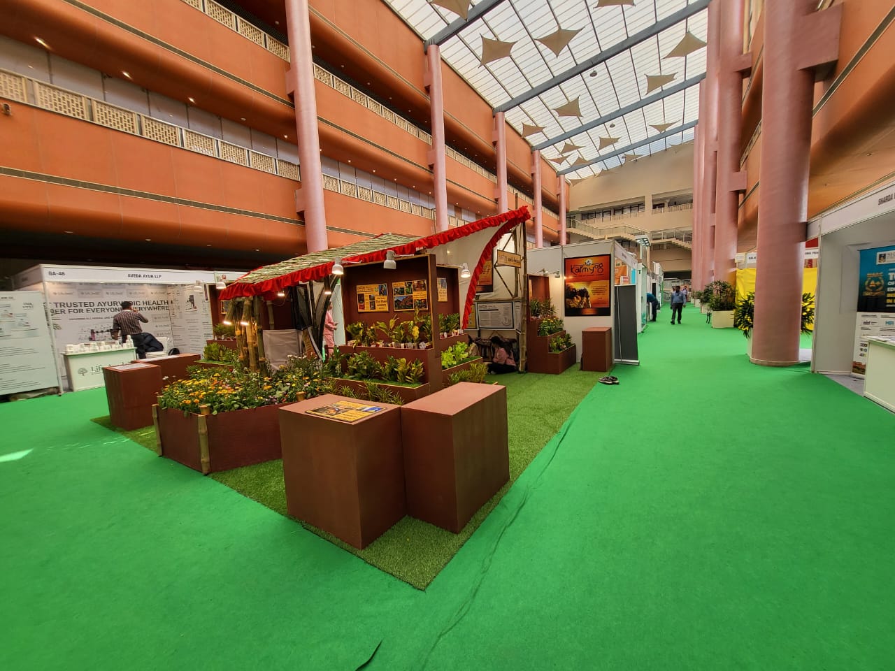 Wide angle of the biophilic stall inside the orange expo hall, contrasting sharply with standard booths around it